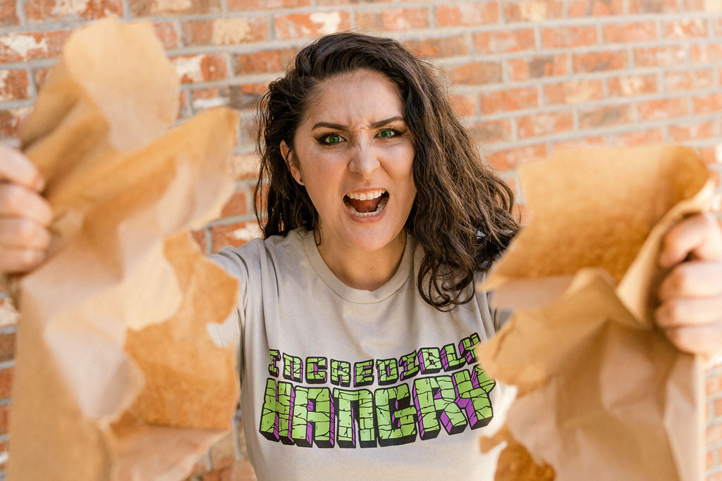 Girl wearing Incredibly Hangry T-shirt ripping bag open