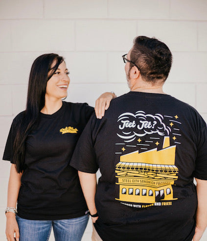 Guy and Girl showing off the Front and back of the Pittsburgh Steel City Sandwich Factory Shirt